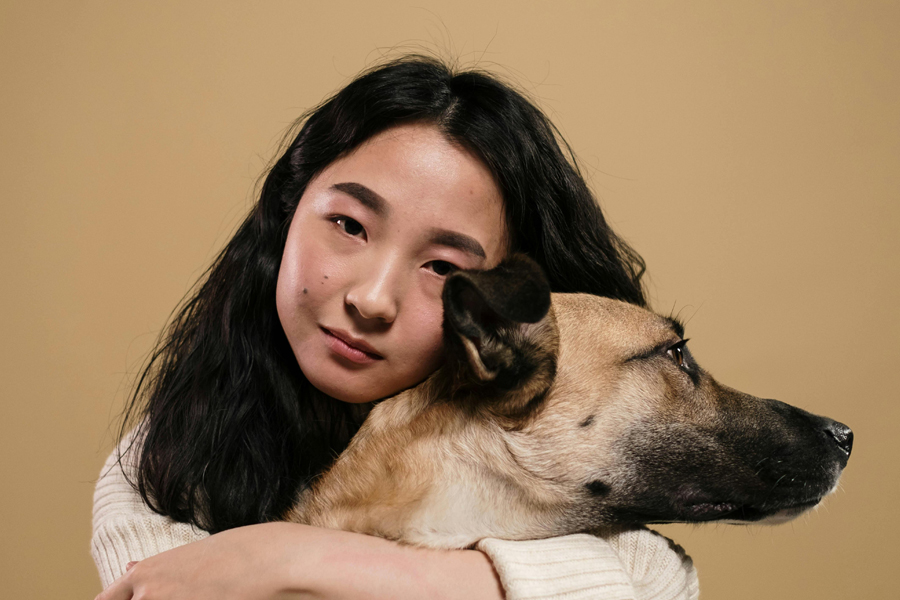 An asian woman with black hair hugs a tan dog with e black muzzle.